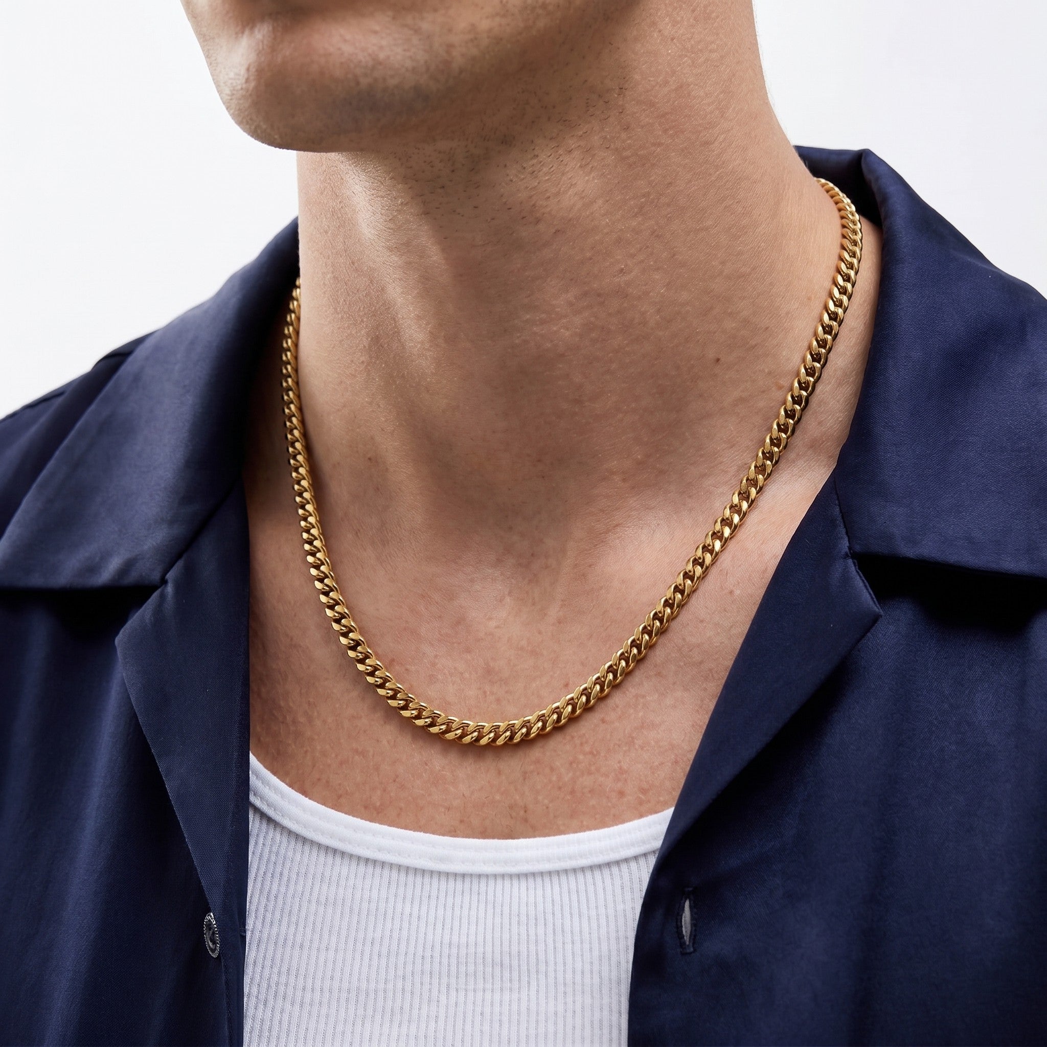 Person wearing a 5mm gold cuban chain necklace with a plain background